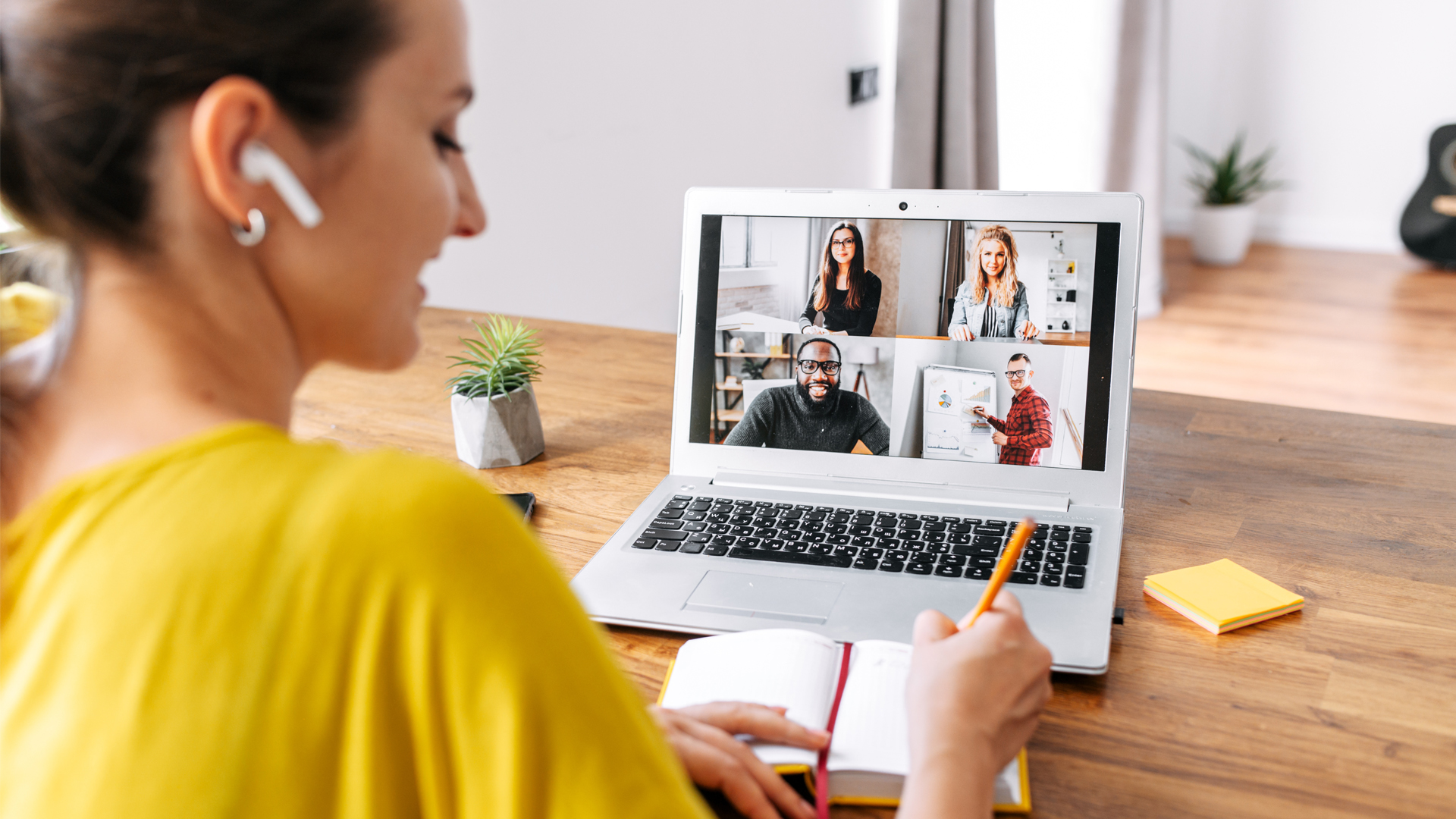 Back view of laptop display with a group of multiracial people on it, young woman watching online webinar and writing notes. Video call, online conference Image